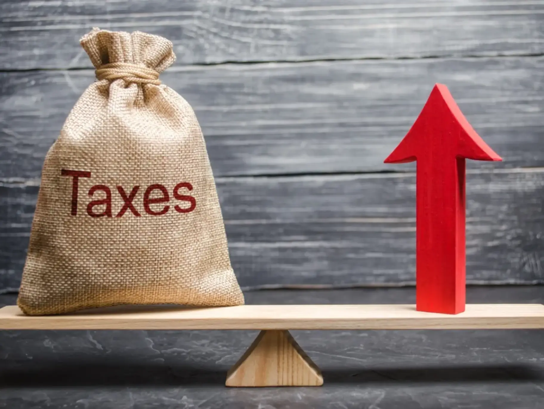 A bag with the inscription taxes and a red arrow up on the scale